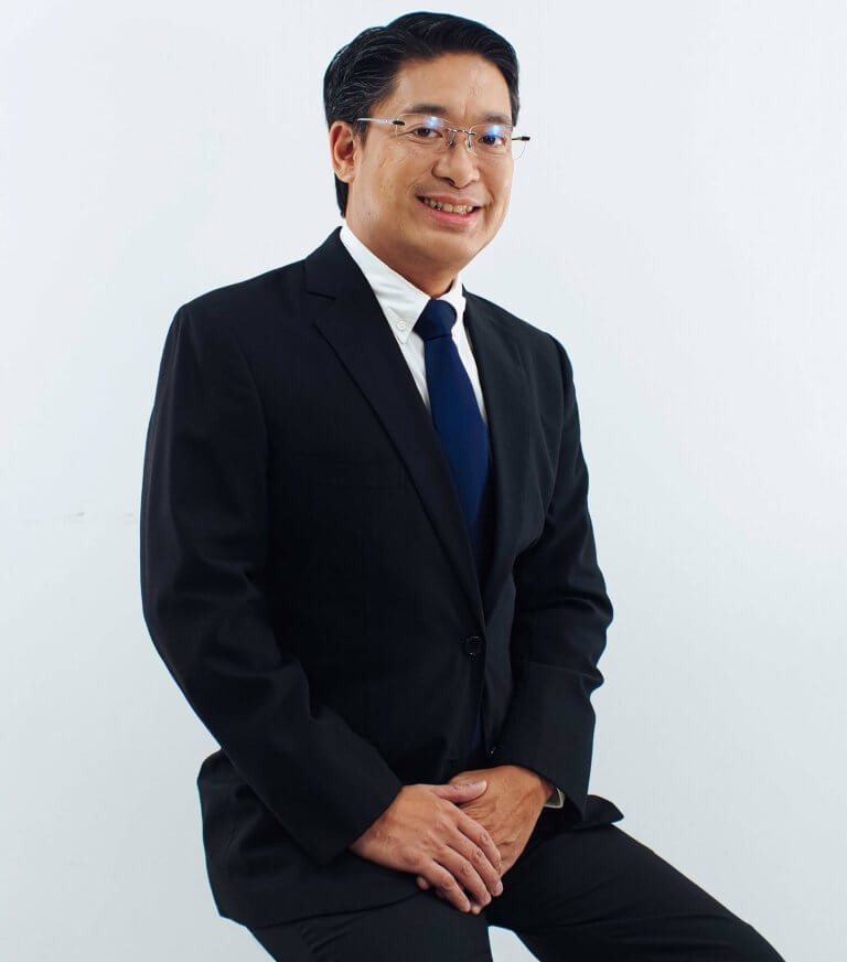 Studio headshot of a smiling male executive wearing glasses and a formal dark business suit.