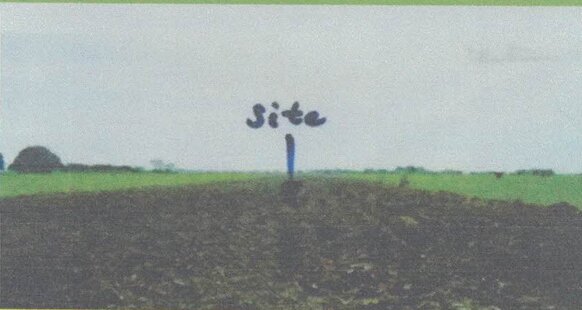 Small blue sign with the word "Site" handwritten on it, placed in a grassy field under a pale sky.