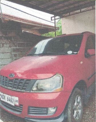 Close-up front view of a red SUV parked under a roofed driveway with its headlights visible.