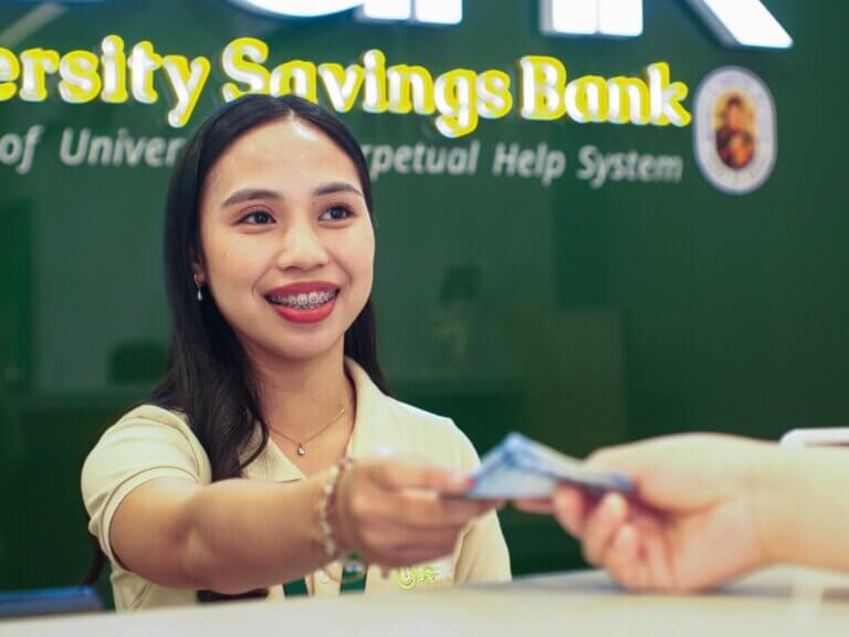 Smiling bank teller processing a cash transaction at a University Savings Bank service counter.